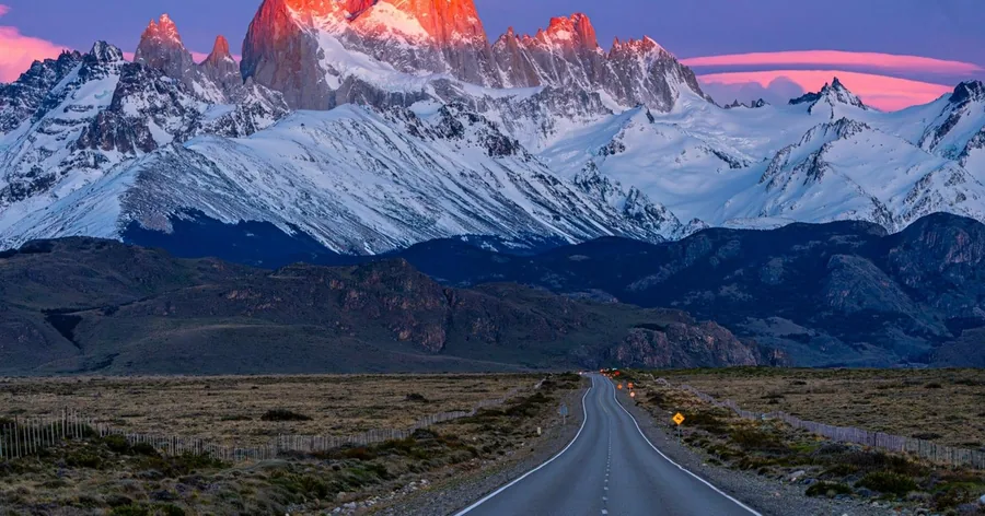 The Fitz Roy massif lit red at dawn above a straight empty road in Patagonia