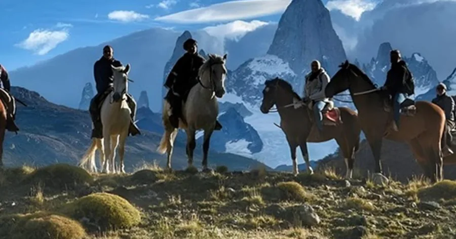 Riders on horseback on a ridge in front of the jagged Fitz Roy range